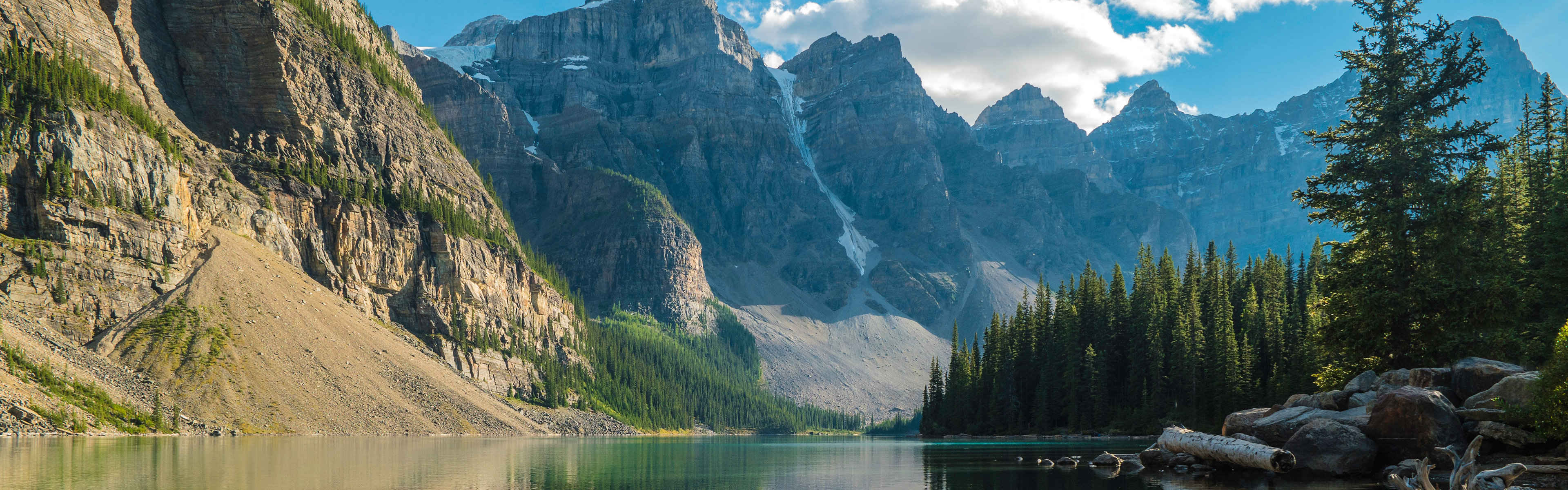 A serene lake nestled between towering, rocky mountains under a clear blue sky with white clouds.