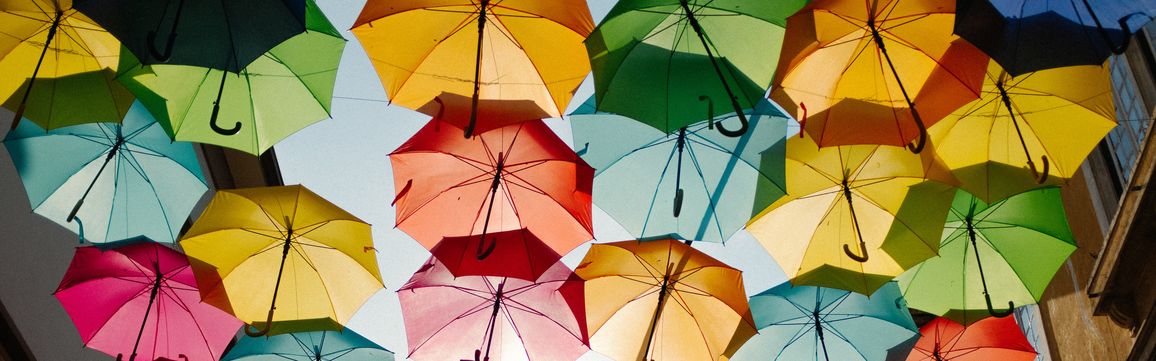 A low-angle view of many colorful open umbrellas, forming a canopy against a bright sky.